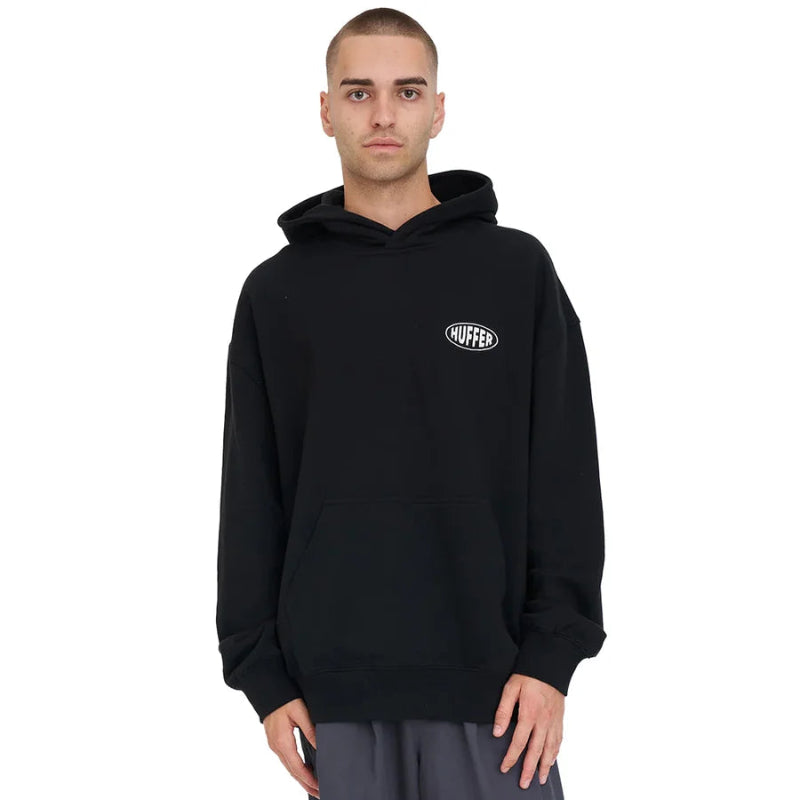 A man wearing a black pullover hoodie with a small white 'HUFFER logo on the left chest, photographed against a solid white background.
