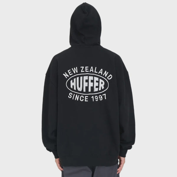 A person shown from the back wearing a black pullover hoodie with a large white graphic on the back reading 'NEW ZEALAND HUFFER SINCE 1997', photographed against a light gray studio background.