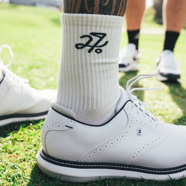 White golf shoe with a sock featuring a logo on a grassy background