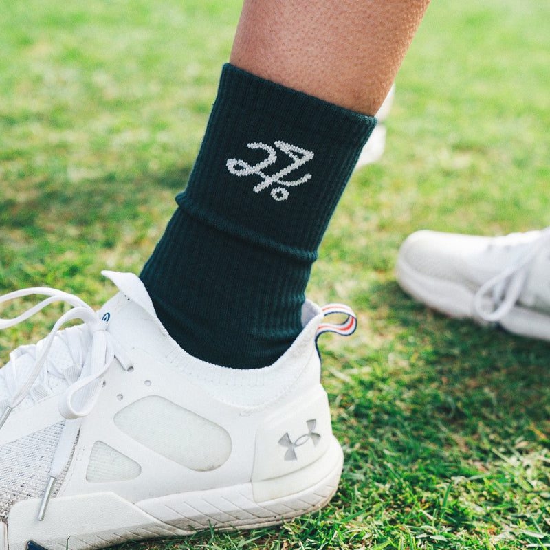 Person wearing green socks with a logo and white sneakers on grass