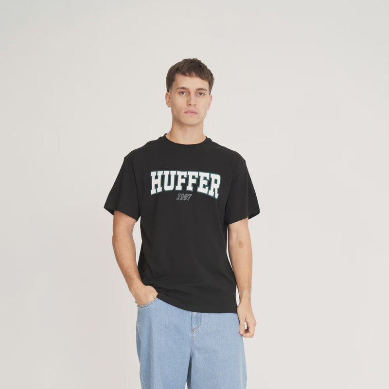 Person wearing a black Huffer t-shirt and light blue shorts on a white background