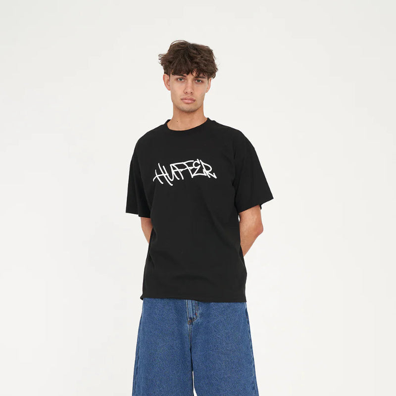 Person wearing a black t-shirt with 'HUFFER' logo and blue shorts on a white background