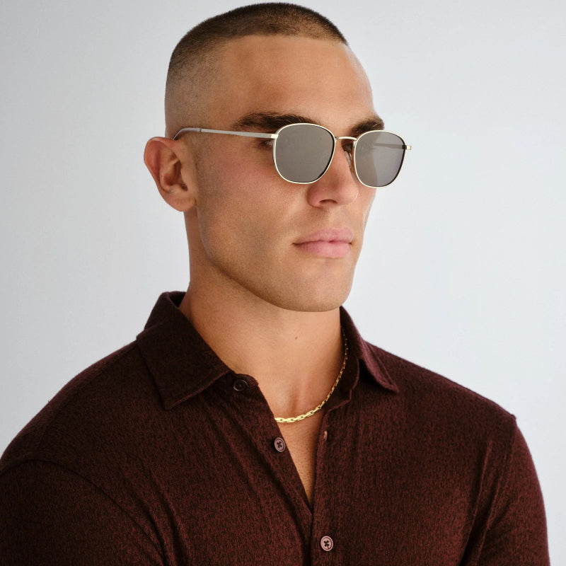 Man wearing sunglasses and a brown shirt against a gray background