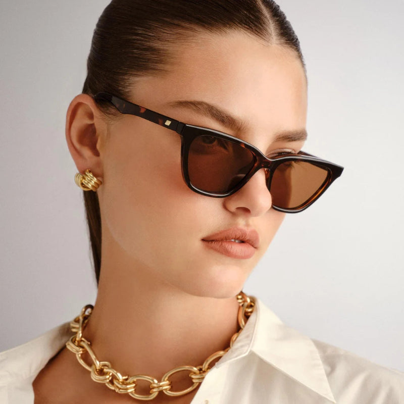 Woman wearing sunglasses and a gold necklace against a neutral background