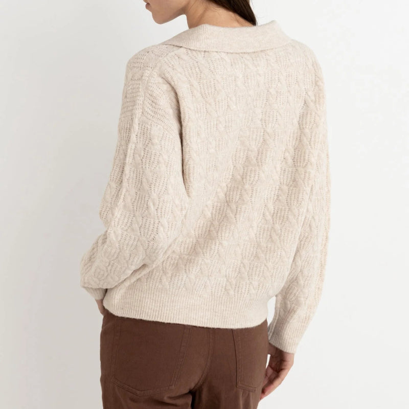 Woman wearing a beige knitted cardigan and brown pants against a white background