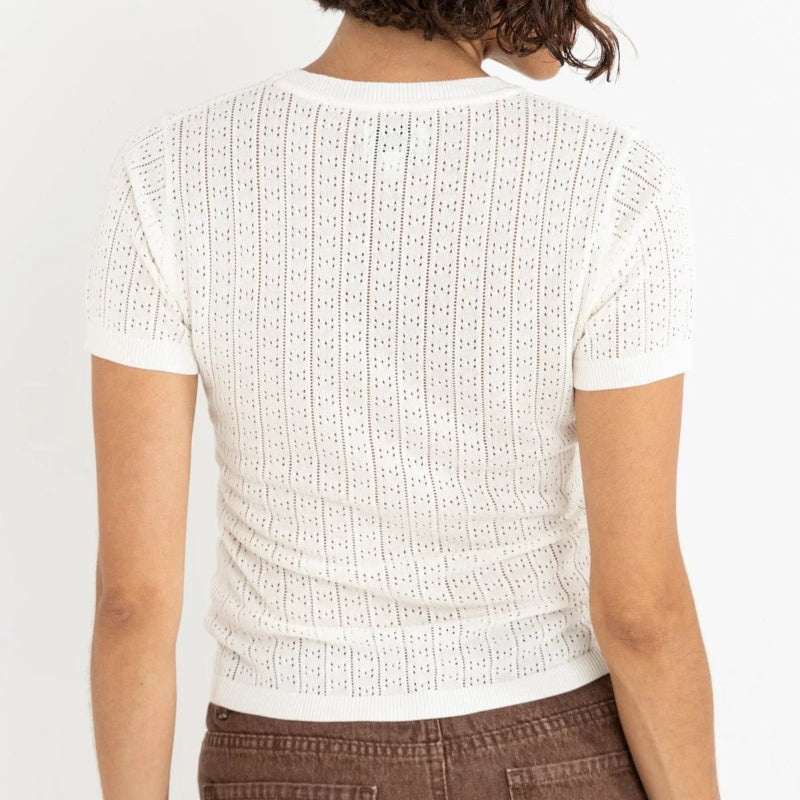 Person wearing a textured white top with brown pants on a plain background