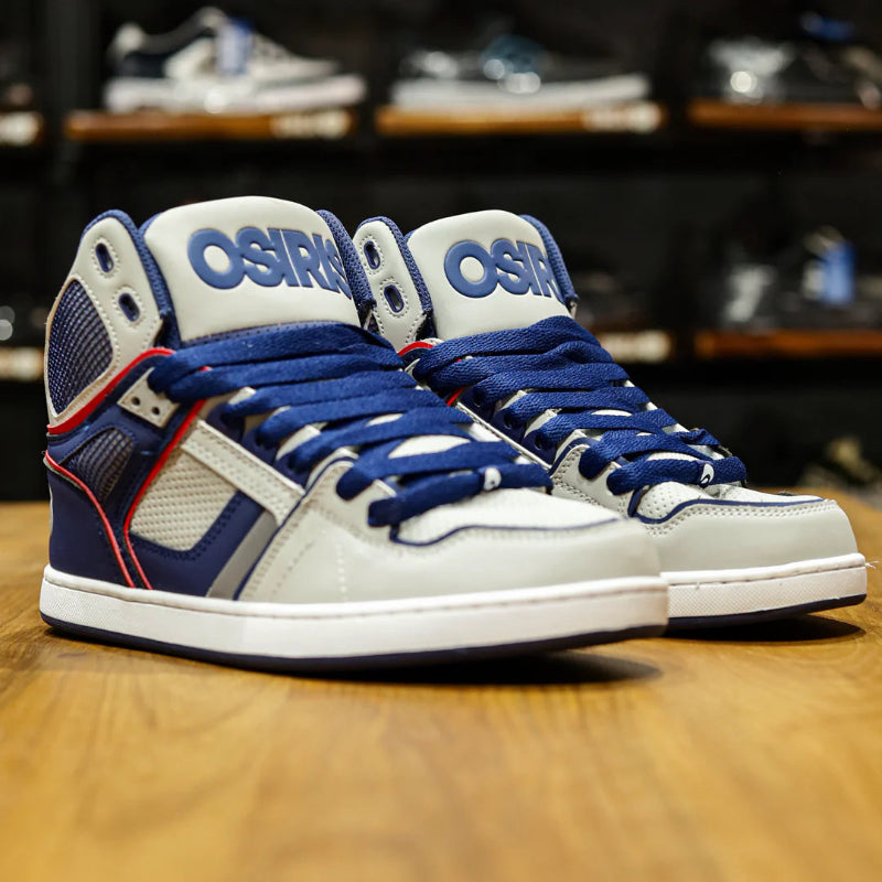 Pair of Osiris high-top sneakers on a wooden floor with shelves in the background.