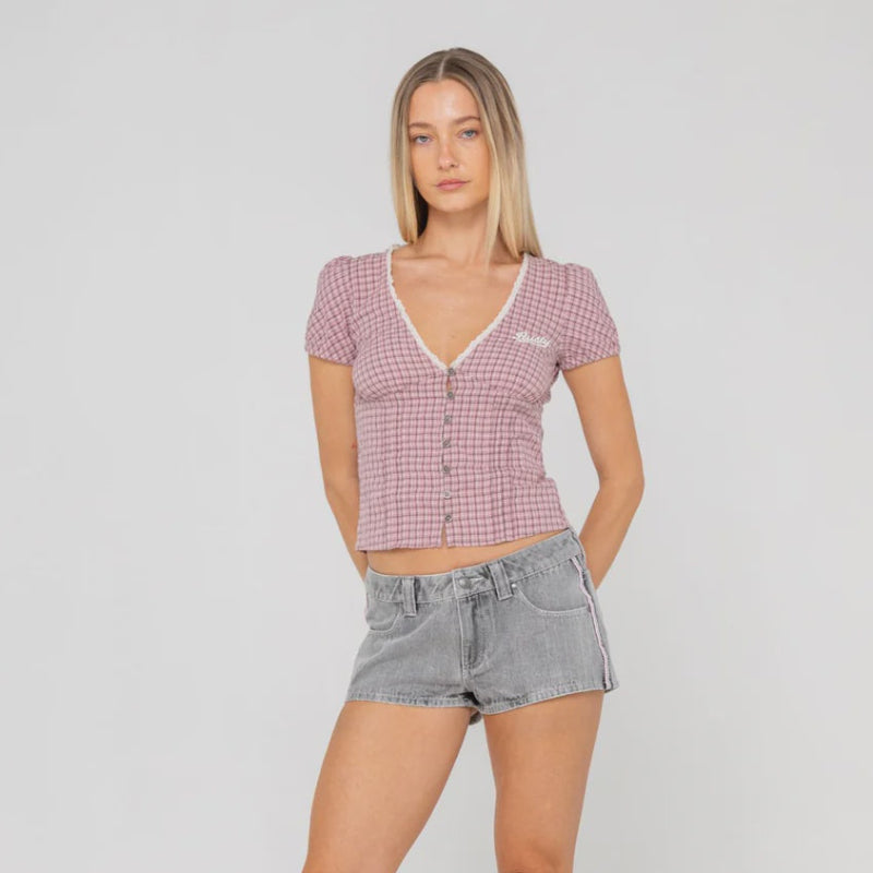 Woman wearing a checkered top, denim shorts, and white cowboy boots on a plain background