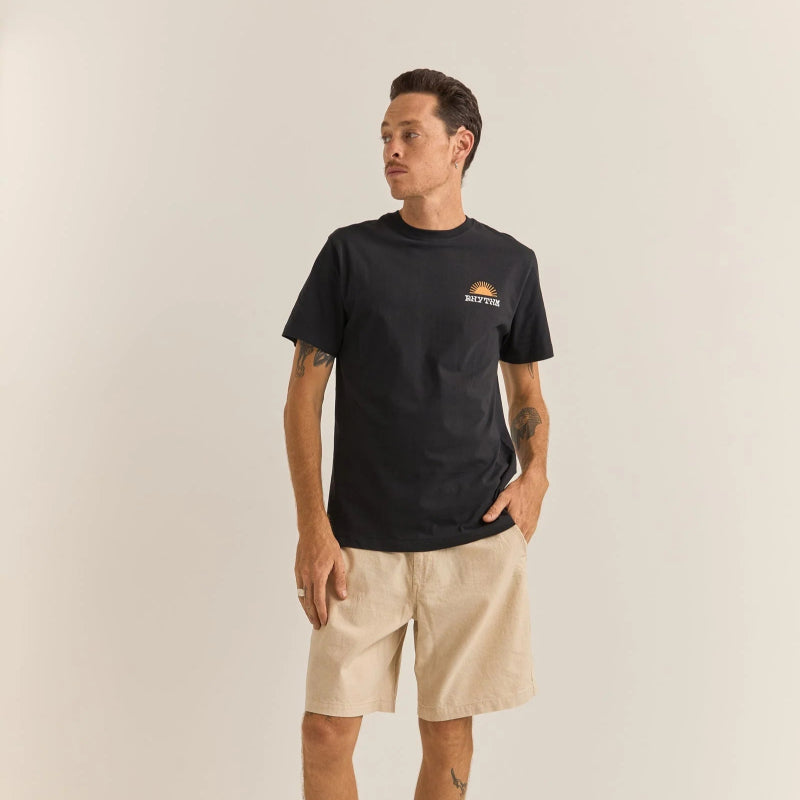 Man wearing a black t-shirt with a logo and beige shorts on a plain background