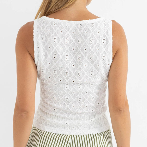 Woman wearing a white sleeveless top with a pattern on a plain background