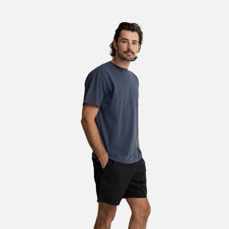 Man wearing a blue t-shirt and black shorts standing against a white background