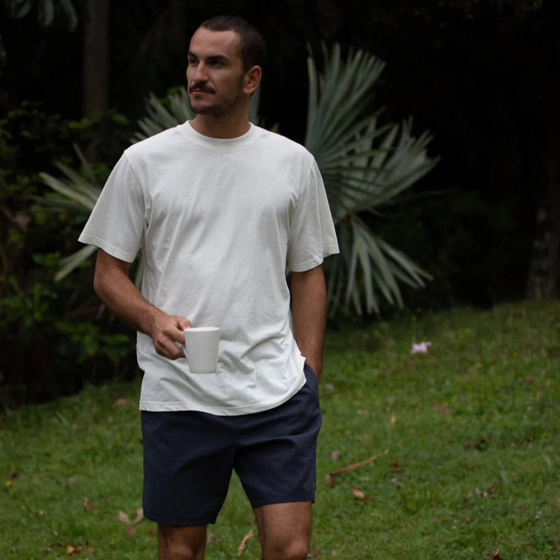 Man in a white t-shirt and navy shorts standing on grass with plants in the background