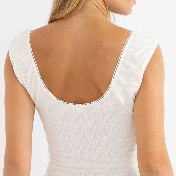 Woman wearing a white sleeveless top with a subtle pattern on a plain background