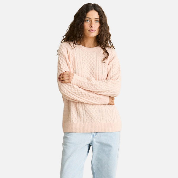 Woman wearing a light pink cable knit sweater and light blue jeans on a white background