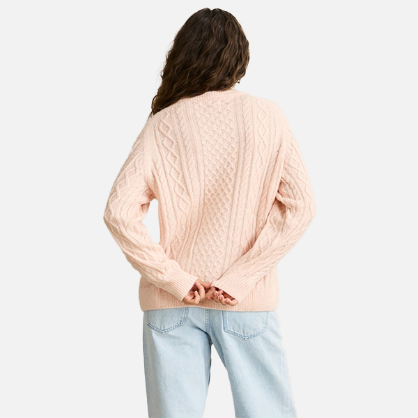 Person wearing a light pink cable knit sweater and light blue jeans on a white background