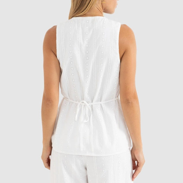 Woman wearing a white sleeveless top and pants on a light gray background