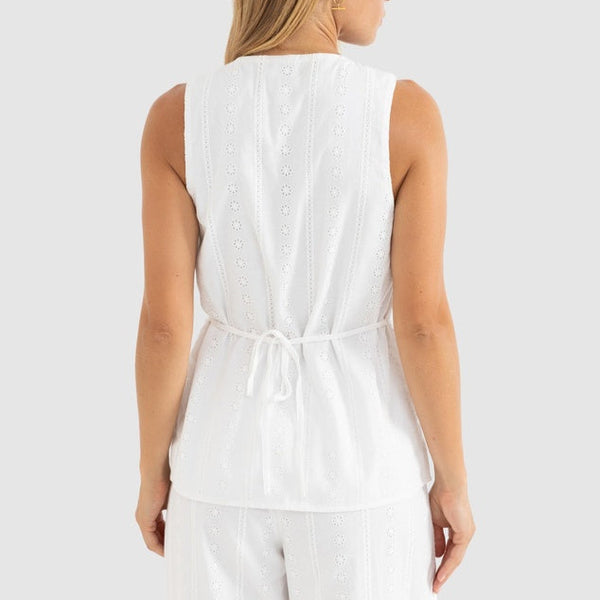 Woman wearing a white sleeveless top and pants on a light gray background