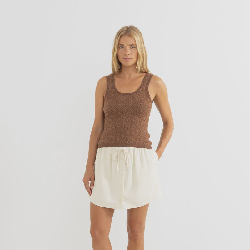 Woman wearing a brown tank top and white shorts on a plain background