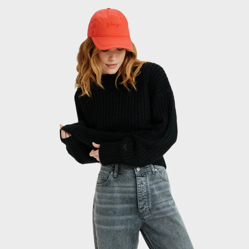 Person wearing a black sweater, gray jeans, and a red cap on a white background