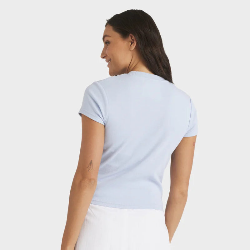 Woman wearing a light blue t-shirt and white skirt on a plain background