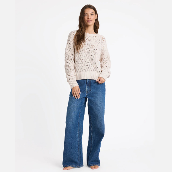 Woman wearing a cream sweater and blue jeans on a white background
