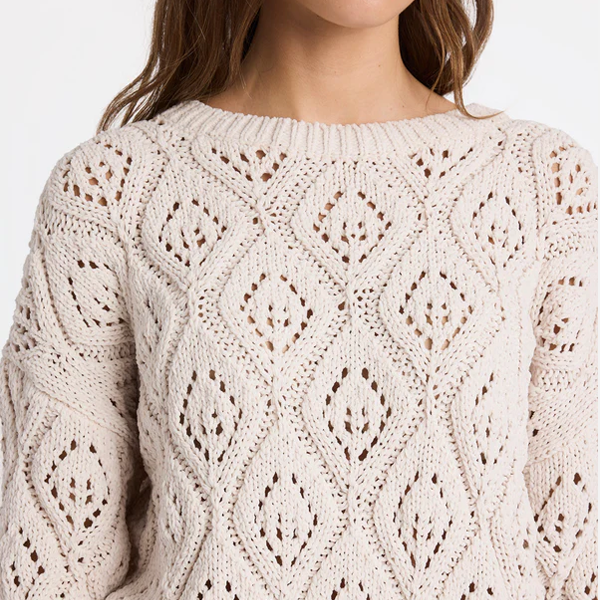 Close-up of a beige knitted sweater with intricate pattern on a white background