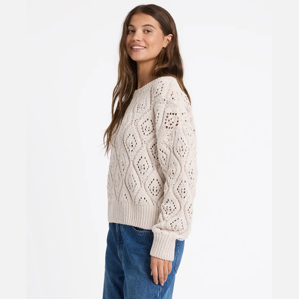 Woman wearing a cream knitted sweater and blue jeans on a white background