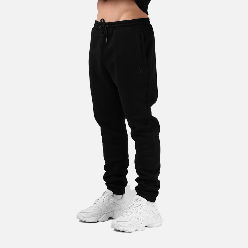 Person wearing black sweatpants and white sneakers on a light gray background