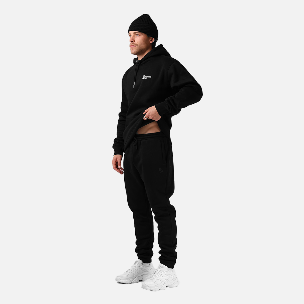 Person wearing a black hoodie and pants with a white background