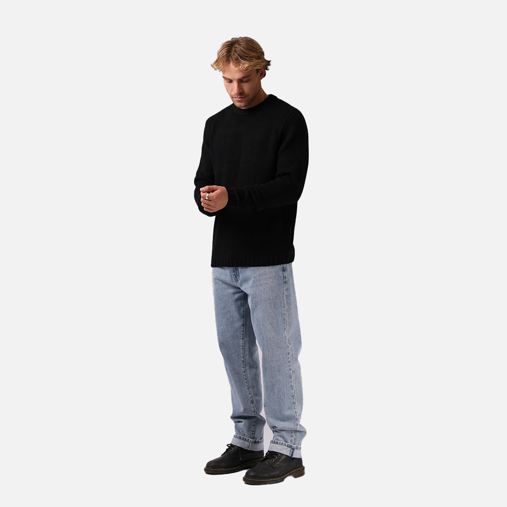 Man wearing a black sweater and light blue jeans on a white background