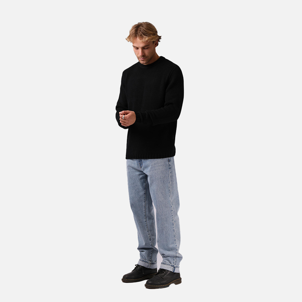Man wearing a black sweater and light blue jeans on a white background