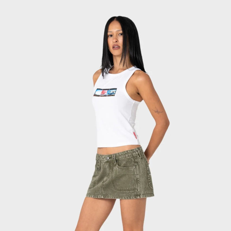 Woman wearing a white tank top with logos and a green denim skirt on a white background