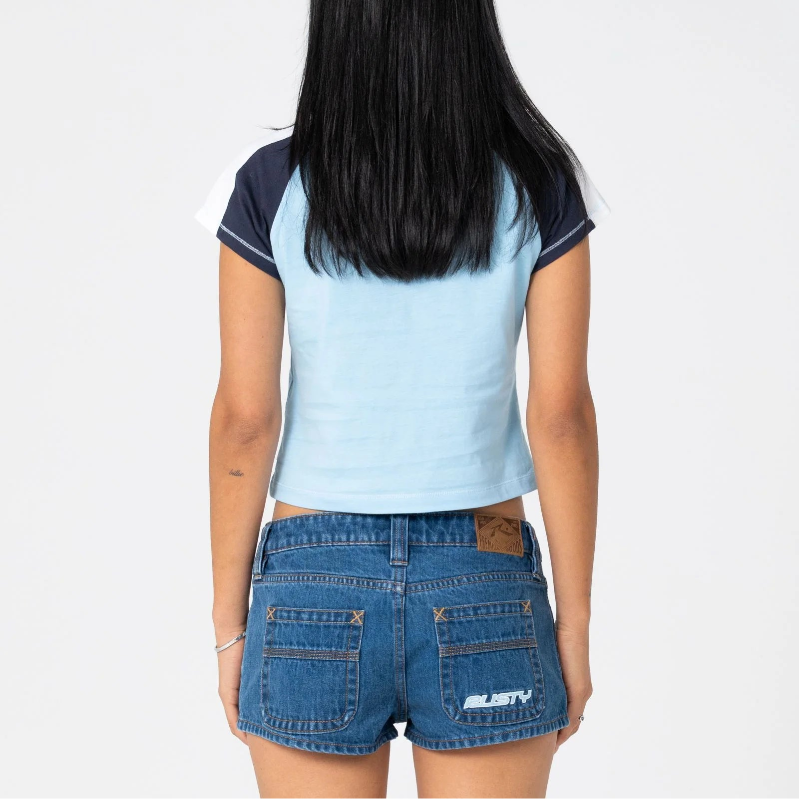 A woman viewed from behind wearing a light blue and navy color-blocked crop top and blue denim shorts against a plain white background.