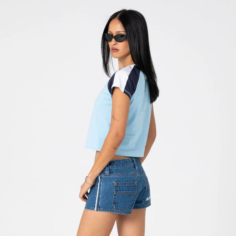 Woman wearing a light blue crop top and denim shorts on a white background