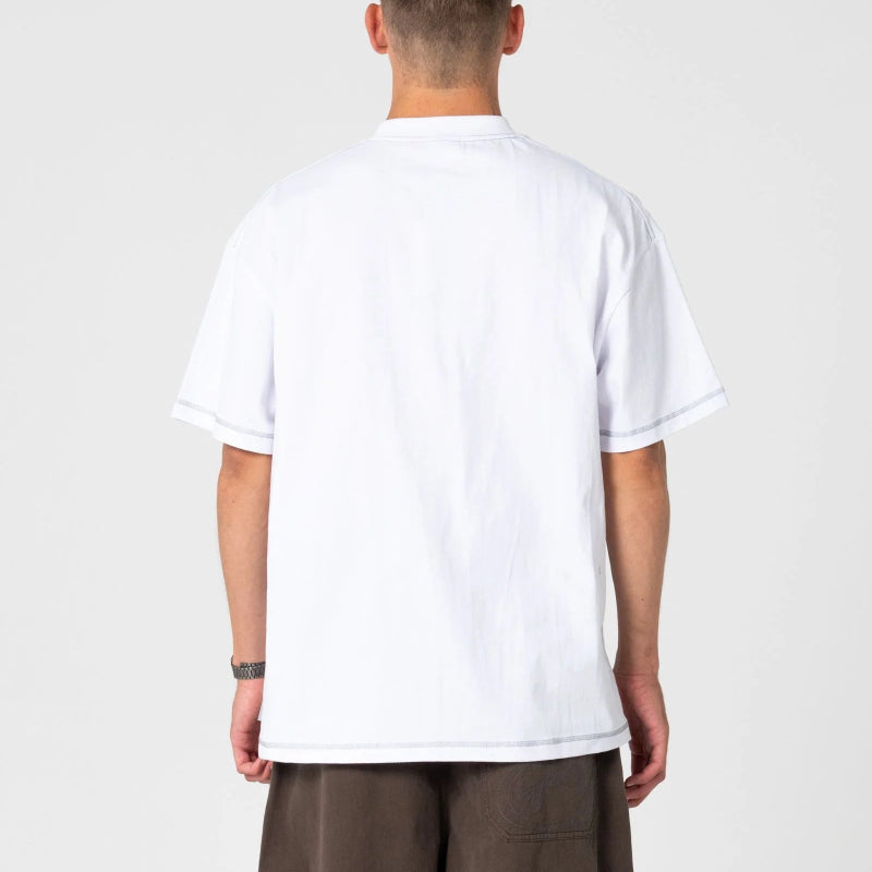 A man viewed from behind wearing a plain white short-sleeve t-shirt and brown pants, standing against a light gray studio background.
