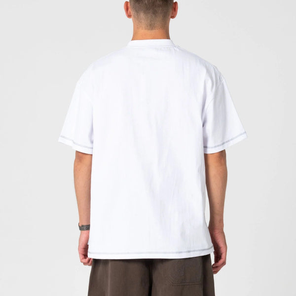 A man viewed from behind wearing a plain white short-sleeve t-shirt and brown pants, standing against a light gray studio background.