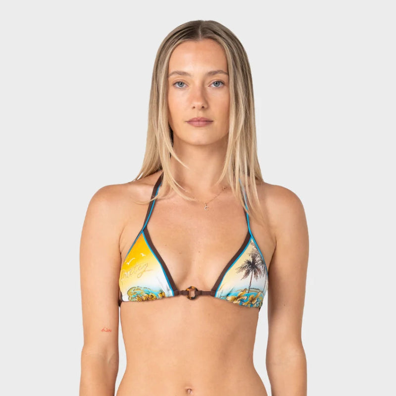 A woman modeling a two-piece bikini against a light gray studio background. The bikini top has a tropical beach print with yellow, blue, green, and brown tones, while the bottom is solid dark brown with thin blue side ties.