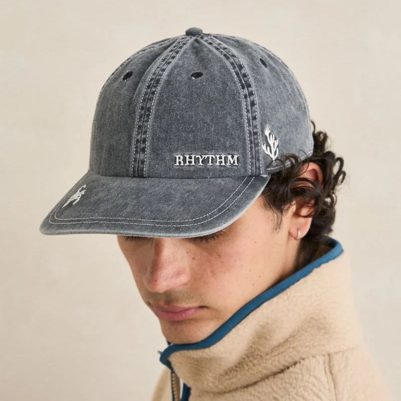 Person wearing a gray cap with 'RHYTHM' branding on a beige background