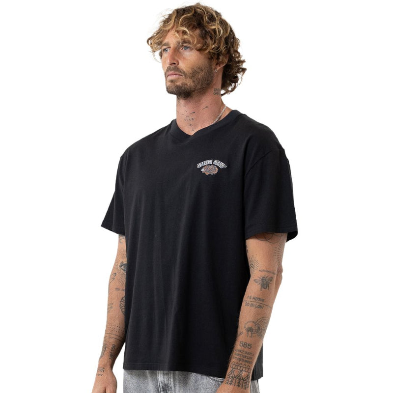 A man wearing a black short-sleeve t-shirt with a small graphic on the left chest, paired with gray sweatpants, photographed against a solid white background.