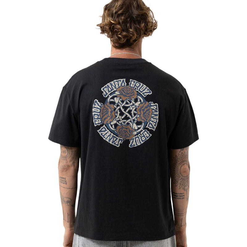 A man viewed from behind wearing a black Santa Cruz t-shirt with a large circular graphic on the back, paired with gray denim shorts.