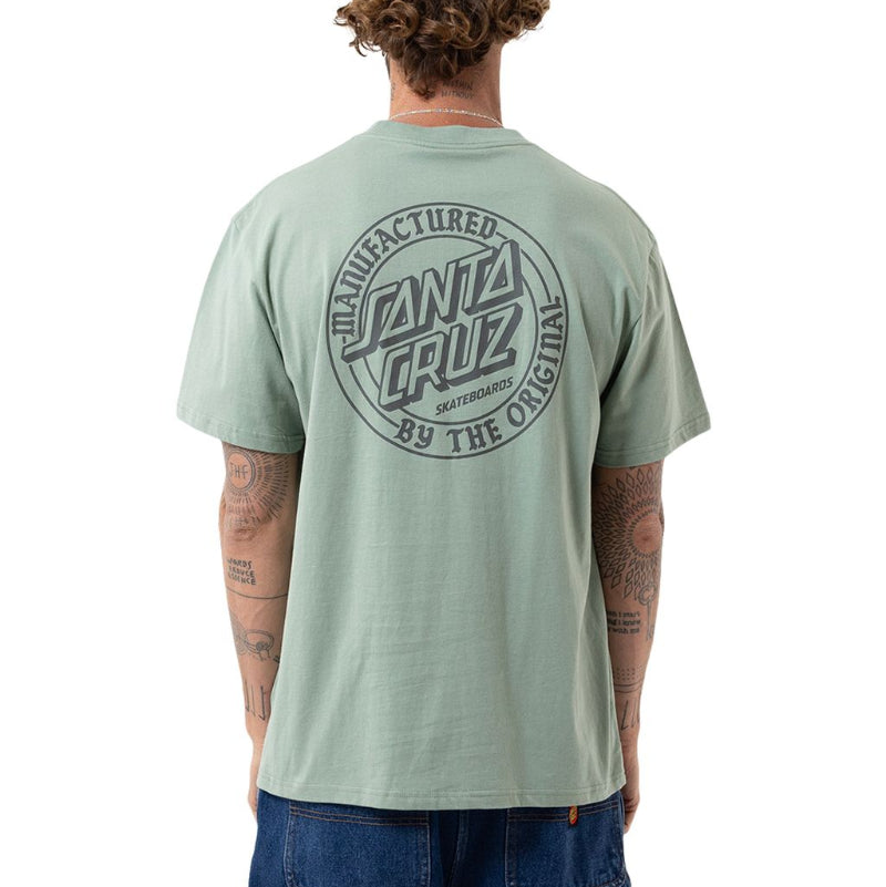 A man viewed from behind wearing a light sage green Santa Cruz t-shirt with a large circular black graphic on the back, paired with blue jeans, against a plain white background.