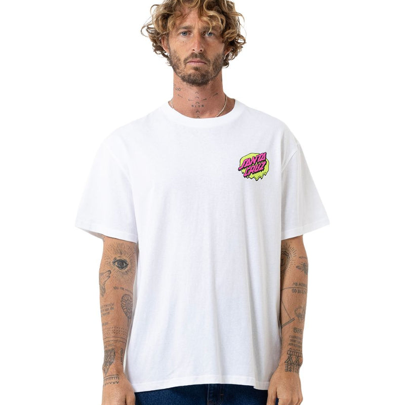 A man with curly hair and tattoos wearing a white crewneck t-shirt with a colorful graphic on the left chest, paired with blue jeans, against a plain white background.