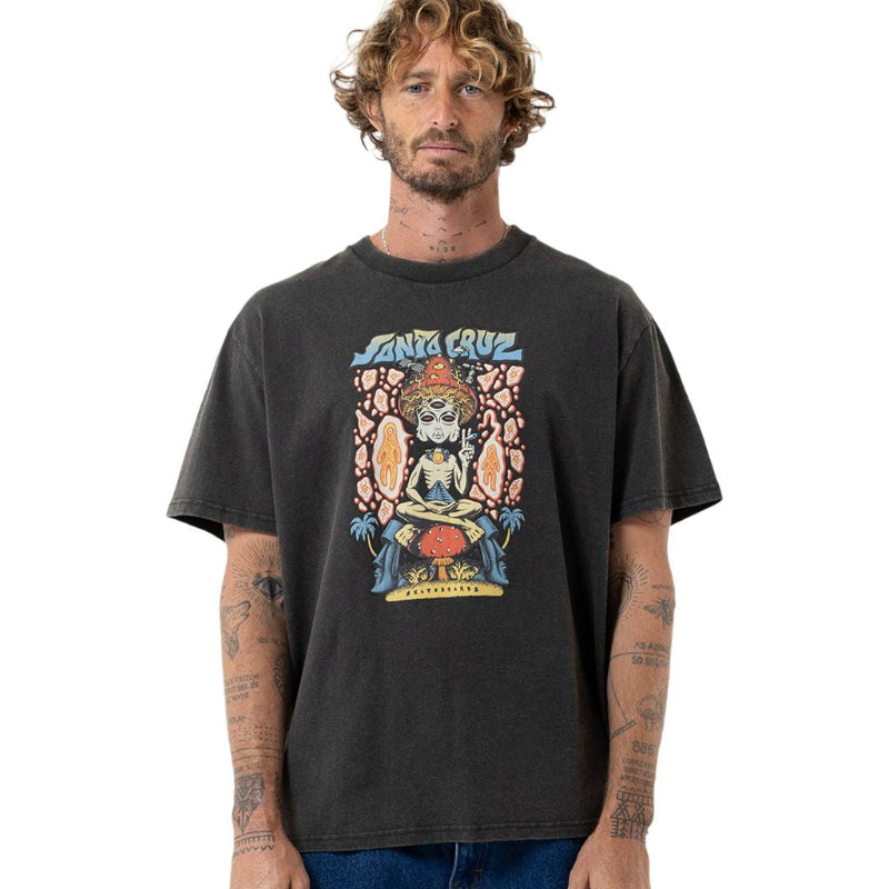 A man wearing a dark charcoal gray graphic t-shirt with a colorful Santa Cruz print, paired with blue jeans, photographed against a solid white background.