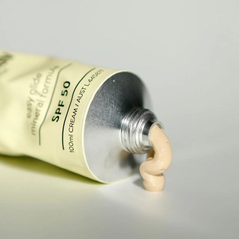 Tube of sunscreen with a small amount of cream oozing out on a neutral background