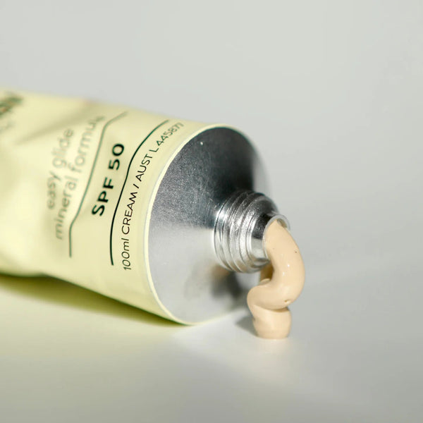 Tube of sunscreen with a small amount of cream oozing out on a neutral background