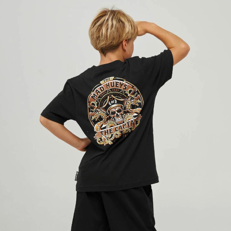 A child model shown from the back wearing a black t-shirt with a large circular graphic print, black shorts, dark gray socks, and black sneakers with white stripes, set against a light gray studio background.