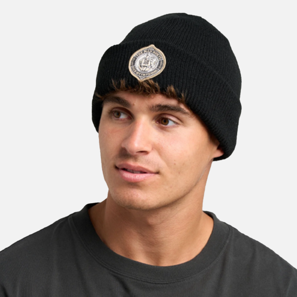 Person wearing a black beanie with a logo on a plain background