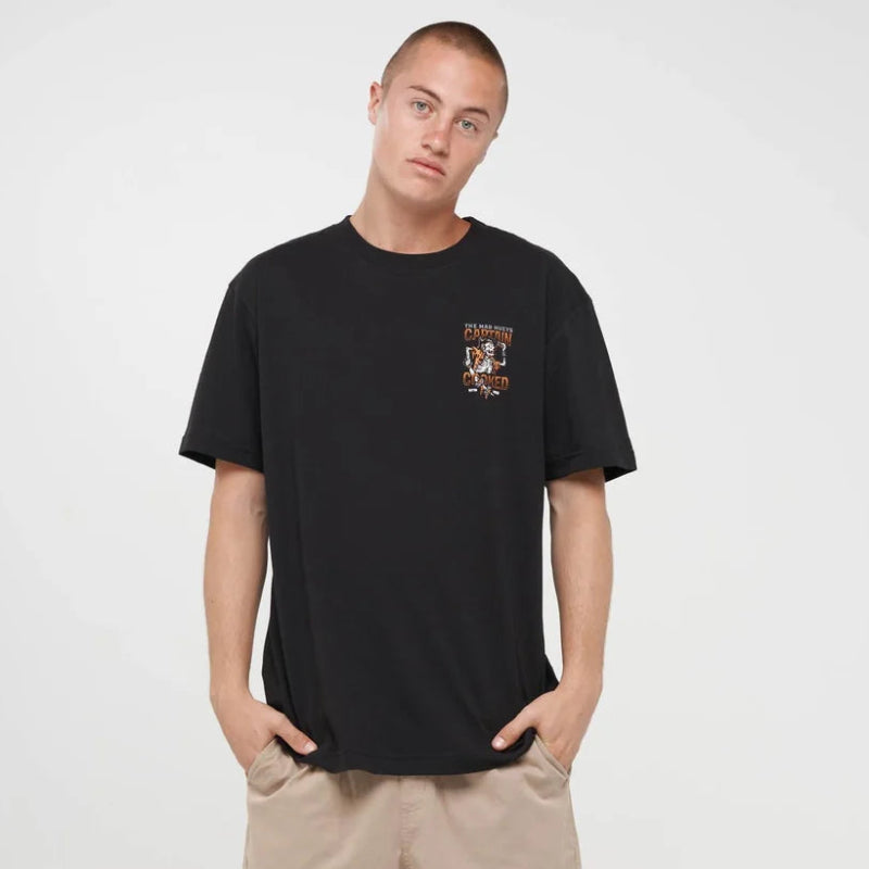 A man modeling a black crewneck t-shirt with a small graphic on the left chest, paired with beige cargo shorts, black socks, and black sneakers, against a plain light gray background.