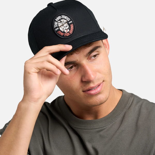 Man wearing a black cap with a logo, adjusting it on a plain background