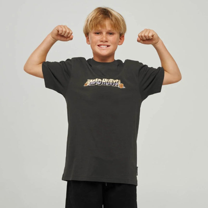 A young boy posing in a black short-sleeve t-shirt with a colorful graphic on the chest, paired with black shorts, gray socks, and black sneakers, against a light gray studio background.